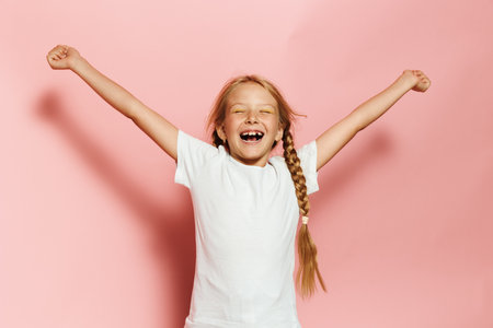 Joyful young girl celebrating with arms up; Excited child pink background
