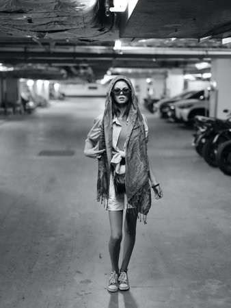 Fashionable Caucasian Female Model Walking Stylishly in the City, Holding a White Bag and Wearing Sunglassesの写真素材