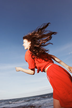 Beach Delight: A Smiling Woman Dancing with Joy in Red Clothes, Enjoying the Freedom of Summer by the Azure Seaの写真素材