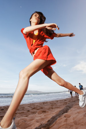 Dancing Freedom by the Sea: A Joyful, Carefree Fashion Model Running on the Beach at Sunset under...