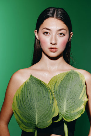 Summer Glamour: A Pretty Lady with Elegant Style, an Attractive Portrait of a Young Female Model with Healthy, Fresh Skin, Wearing a White Dress, Posing outdoors against a Green Background, her Brunette Hair Adorned with Red Leaves.の写真素材