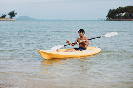 Happy Asian Man Kayaking in Tropical Paradise: Fun-filled Beach Vacation Adventureの写真素材