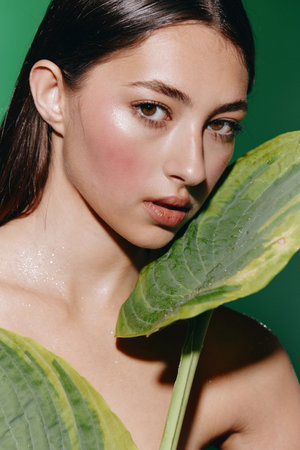 Beauty Woman Portrait with Attractive Young Female Face and Fashionable Green Leaf Backgroundの写真素材