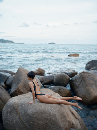 Exquisite Summer: A Sensual Swimwear Model Posing on a Rock, Surrounded by Sand and Crystal-clear Ocean Watersの写真素材