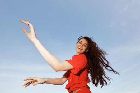 Beach Bliss: Smiling woman enjoying freedom and joy under the summer sun, dancing on the sandy beach in vibrant red fashion clothes against the backdrop of a beautiful blue sky and tranquil sea.の写真素材