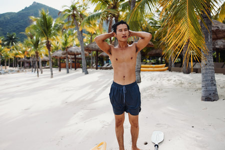 Smiling Asian Man with Muscular Torso Enjoying Summer Vacation on a Tropical Beachの写真素材