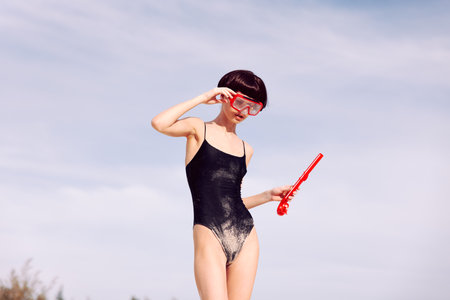 Smiling woman snorkeling in a red fashion swimsuit, wearing a tropical-themed mask and looking at the camera with joyの写真素材