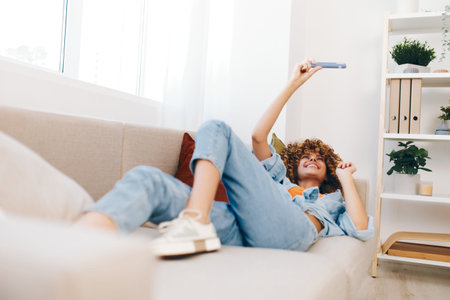 Happy Woman Holding Mobile Phone on Cozy Sofa at Homeの写真素材
