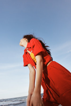 Smiling Woman Dancing in Red Clothes on a Sunny Beach, Embracing the Freedom and Joy of Summerの写真素材