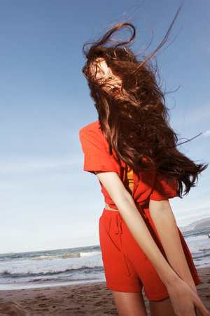 Smiling Woman Dancing for Joy on Sunny Beach, Enjoying Freedom and Summer Vacation in Fashionable Red Clothesの写真素材