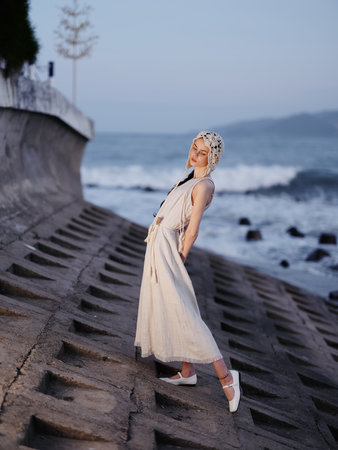 Summer Beauty: A Young Woman in a Blue Dress, Enjoying the Tropical Breeze and Serene Ocean Viewの写真素材