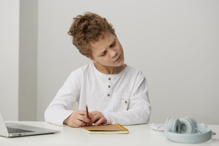 Smiling boy using laptop for elearning at home, enjoying online education and playing educational games He sits at a table, surrounded by books and notebooks, fully engaged in his virtual study Withの写真素材