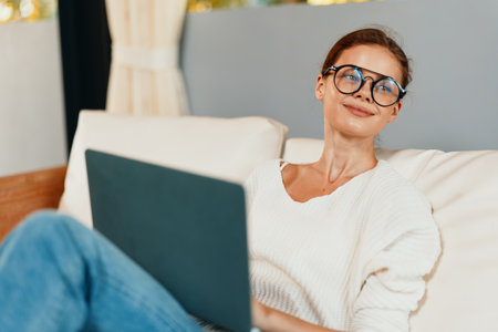 Woman working from home on her laptop, sitting comfortably on a couch in a modern and stylish home office She is a freelancer or a businesswoman, using technology and the internet to run her startupの写真素材