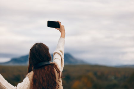 Mountain Adventures: A Smiling Woman Captures her Freedom and Nature Exploration with a Smartphone Selfieの写真素材