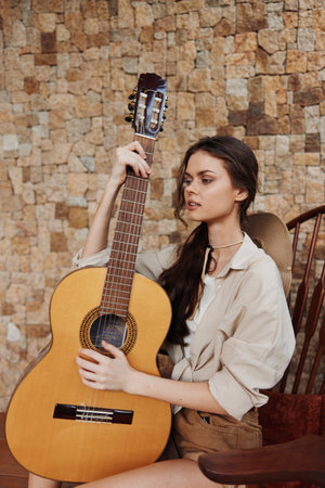 A woman sitting on a chair holding an acoustic guitar in front of a brick wallの写真素材