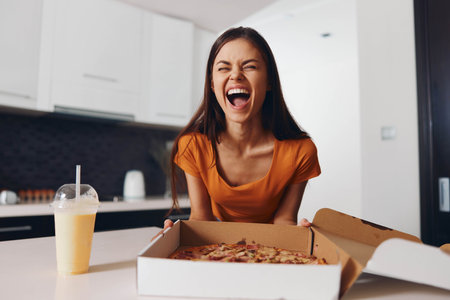 Woman enjoying a delicious slice of pizza and refreshing glass of juice at homeの写真素材