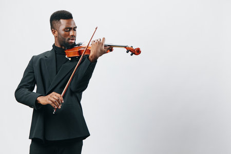 Talented young African American man in stylish black suit playing violin with passion, isolated on white backgroundの写真素材
