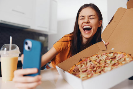 Woman taking a selfie with a slice of pizza in her hand and a pizza box in front of herの写真素材
