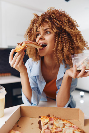 Curlyhaired woman enjoying a delicious slice of pizza in front of a tempting box of pizzaの写真素材