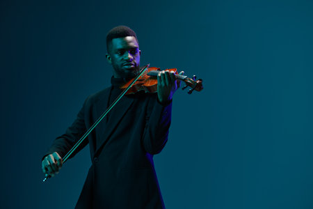 African American man wearing a black suit playing the violin against a vibrant blue backgroundの写真素材
