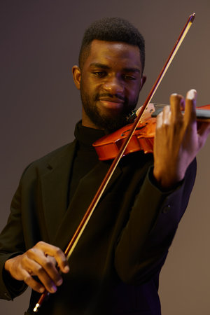 Classically Dressed Man Holding Violin Smiling Against Black Background In Elegant Portrait Shotの写真素材