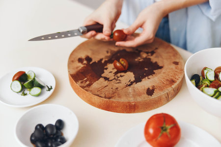 Woman preparing meal with fresh tomatoes and vegetables on wooden cutting board in domestic kitchen settingの写真素材