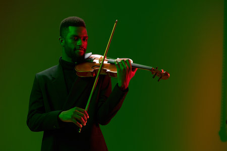 Elegant man in formal attire playing violin in front of vibrant green and red backgroundの写真素材