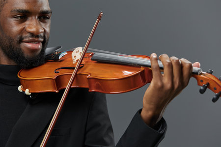 African American man in black suit playing violin on gray background, creating soulful music atmosphereの写真素材