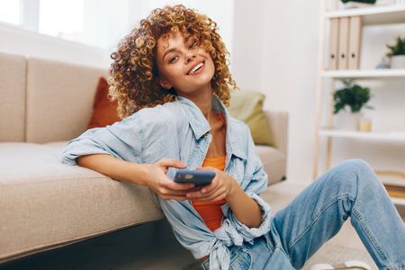 Smiling Woman Holding Mobile Phone on Cozy Sofa in Living Roomの写真素材