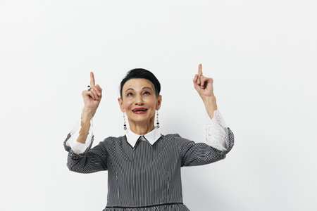 Happy elderly woman in a floral dress with arms raised in joyful celebration and a beaming smile on...