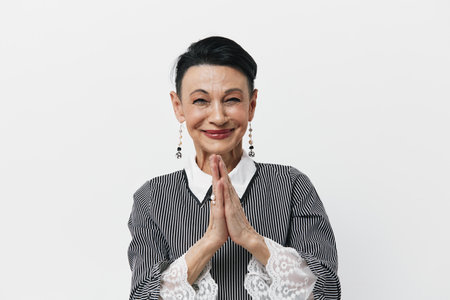 Portrait of an elderly woman expressing joy and appreciation by clapping hands against a white backdropの写真素材