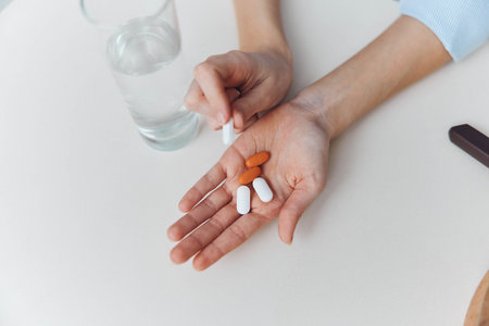 Womans hands holding pills and glass of water on white table Healthcare, medication, treatment conceptの写真素材