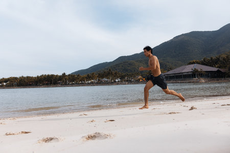 Muscular Asian Athlete Feeling the Freedom of Outdoor Cardio Workout on the Beach at Sunsetの写真素材