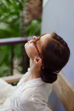 Happy woman standing on a tropical balcony, enjoying a relaxing vacation in a trendy apartment She smiles, basking in the warm sunlight, embracing the freedom and joy of a peaceful morning Withの写真素材