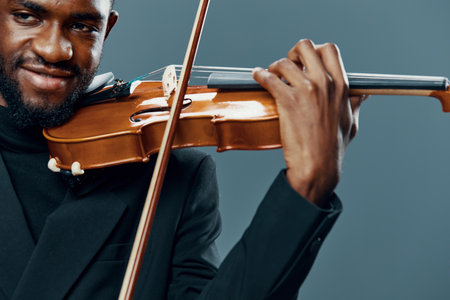 Elegant african american man playing violin in tuxedo on gray background for artistic music performance conceptの写真素材