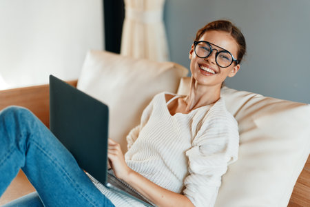 Smiling Woman Working from Home on Laptop in Modern Indoor Setting with a Comfortable Couchの写真素材