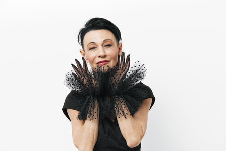 Mysterious woman in elegant black dress and gloves posing with hands on face in dramatic fashion...