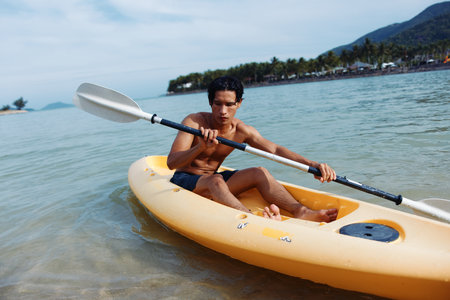 Joyful Asian Man Kayaking on a Tropical Beach, Enjoying a Summer Vacation Adventure