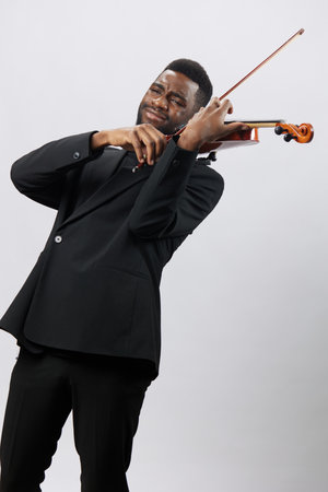 Elegant African American Man in Tuxedo Playing Violin on White Background Musical Performance Concept Photoの写真素材