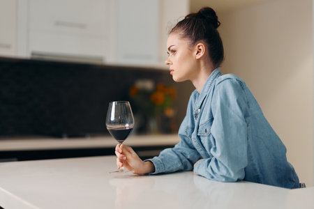 Wine and Loneliness: A Depressed Woman Drinking Alone in a Modern Kitchenの写真素材
