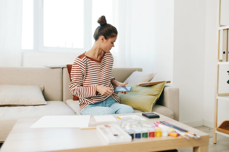 Happy Teenage Girl, a Creative Artist, Painting a Cute Portrait on the Sofa in her Modern Home Studioの写真素材