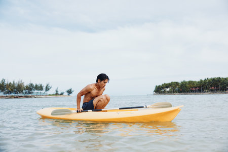 Kayaking Adventure: A Happy Asian Man Enjoying a Summer Vacation on a Tropical Beach, Paddling a Kayak with an Oar in Handの写真素材