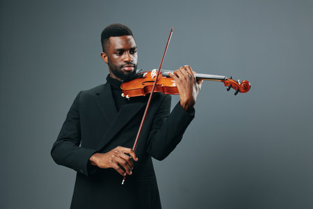 Elegant African American male musician in black suit playing violin against gray background, creating soulful melodiesの写真素材