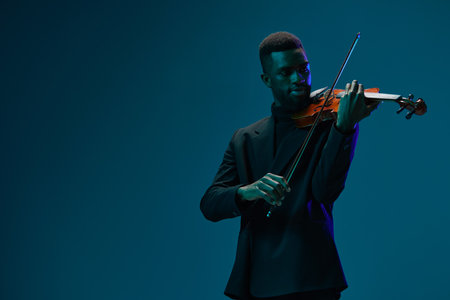 Elegant man in black suit playing violin on blue background with copy space for music conceptの写真素材