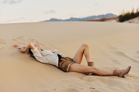 Woman laying on sand in desert with legs up in air under blue sky on sunny dayの写真素材