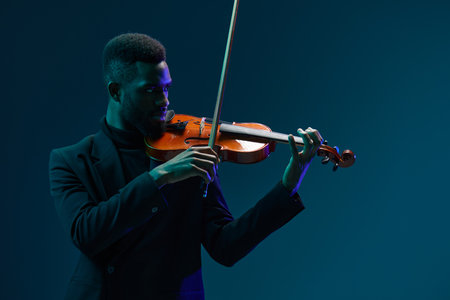Man in suit playing violin in dramatic lighting against dark background creating a captivating musical performance atmosphereの写真素材