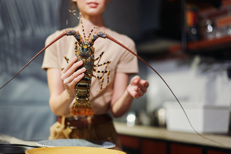 Woman holding lobster on plate in kitchen with knife and fork, preparing delicious seafood mealの写真素材