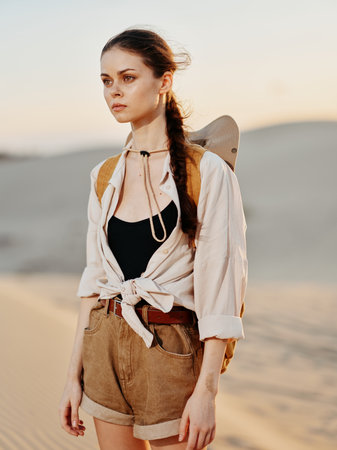 Serene young woman standing on sandy dunes in stylish shorts and shirt on sunny day