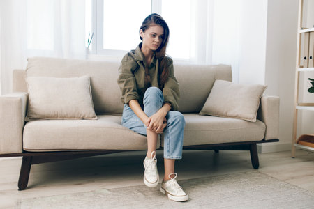 Sad and Worried Woman Sitting on a Couch, Expressing Despair and Mental Health Crisis at Homeの写真素材