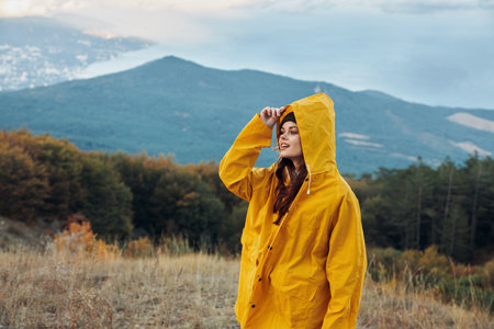A woman in a yellow raincoat enjoying the scenic beauty of mountains while standing on a hillの写真素材